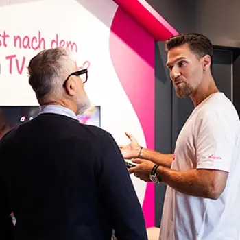 Beratungsgespräch am Messestand: Mitarbeiter erklärt TV-Angebot einem Kunden