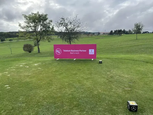 Werbebanner von Telekom Business Partner Bad Urach auf gepflegtem Golfplatz bei Wolkenhimmel.
