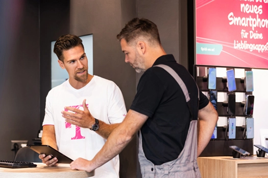 Verkäufer berät Kunden im Handyshop zu Smartphones, Tablet in der Hand